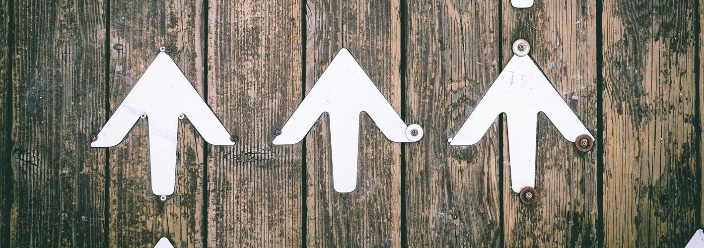 several white arrows pointed up painted on a wooden fene